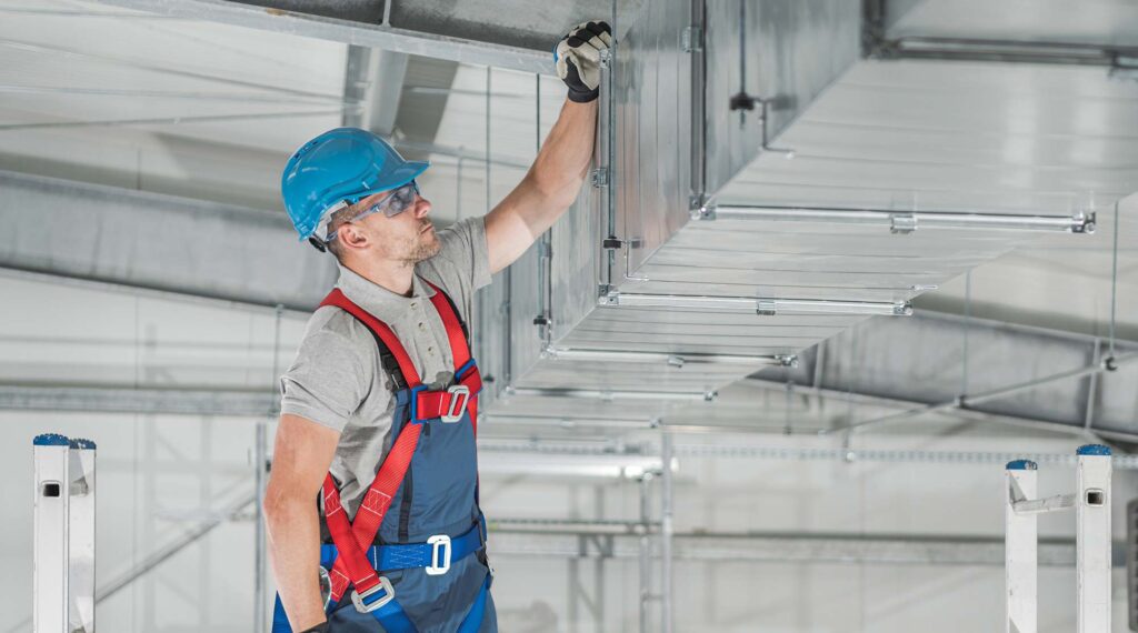 An HVAC service worker inspects ductwork.